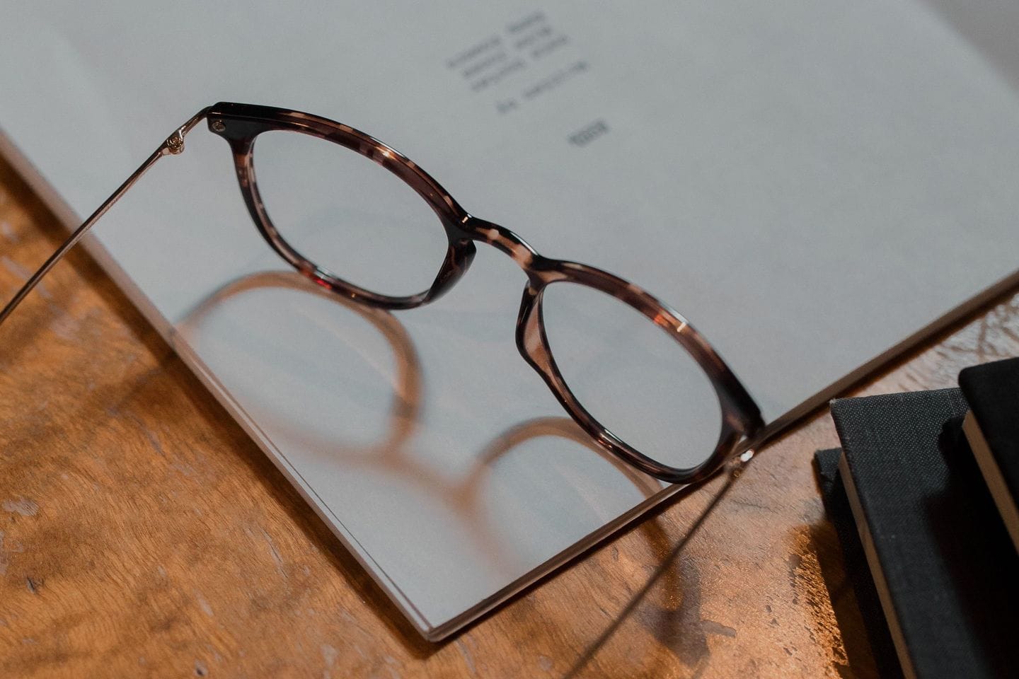 Lesebrille liegt auf einem aufgeschlagenen Manuskript auf einem hölzernen Schreibtisch, daneben gebundene Hefte