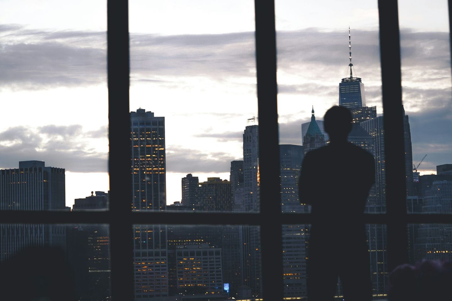Silhouette einer Person am Fenster vor einer Hochhaus-Skyline in der Dämmerung