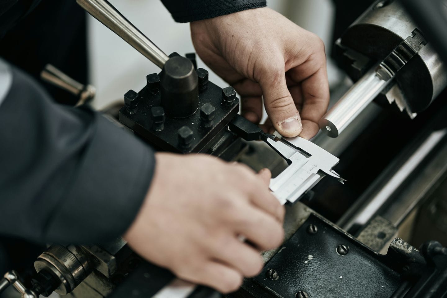 Hände prüfen mit einem Messschieber ein Werkstück an einer Drehmaschine