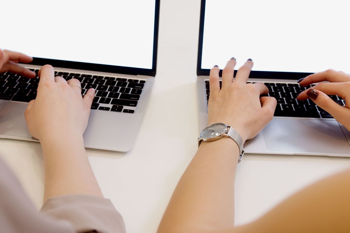 Zwei Personen arbeiten nebeneinander an Laptops, nur Hände und Unterarme im Bild